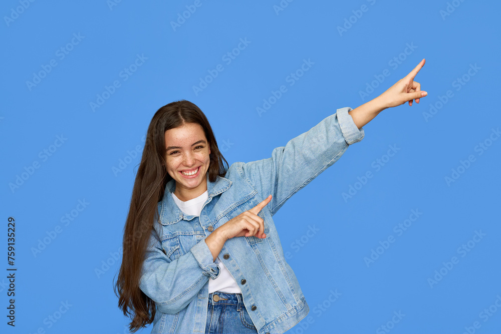 Smiling pretty freckled gen z brunette Latin girl, cute cheerful happy Hispanic teen student wearing denim outfit looking at camera pointing aside at copy space standing isolated on blue background. Smiling pretty freckled gen z brunette Latin girl, cute cheerful happy Hispanic teen student wearing denim outfit looking at camera pointing aside at copy space standing isolated on blue background.