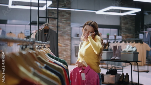 Excited shopaholic calling smartphone choosing clothes in shop mall closeup