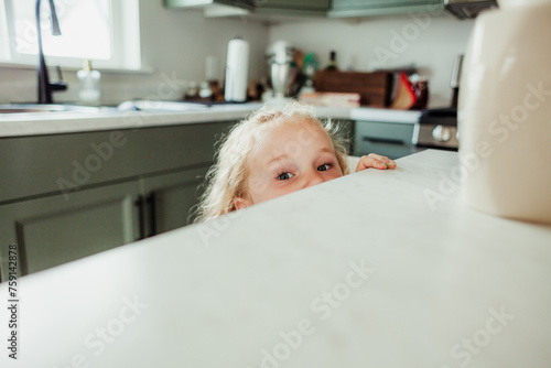 Child peeks over the edge of the kitchen counter. photo