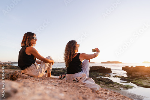 two women taking a selfie with their cell phone at sunset photo