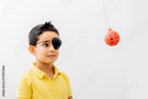 Boy wearing medical eye patch looking at therapy ball photo