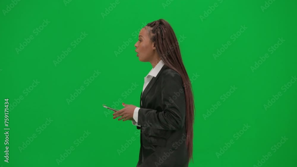 Female reporter isolated on chroma key green screen background. African American woman news host in suit walking and talking, holding tablet Side view. Female reporter isolated on chroma key green screen background. African American woman news host in suit walking and talking, holding tablet Side view.