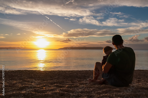 Father with small child enjoying romantic sunset at beach in town Makarska, Split-Dalmatia, Croatia, Europe. Coastline of Makarska Riviera, Adriatic Sea. Dreamlike atmosphere. Family vacation concept photo