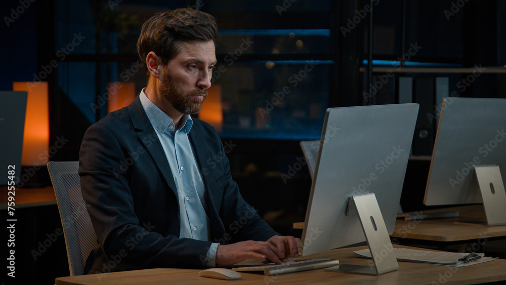 Male business portrait confident focused businessman millennial caucasian senior 40s adult man chief boss leader sit at desk with computer search online data working alone in evening office indoors Male business portrait confident focused businessman millennial caucasian senior 40s adult man chief boss leader sit at desk with computer search online data working alone in evening office indoors