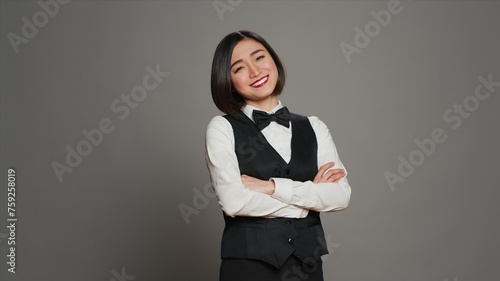 Asian receptionist posing with arms crossed on camera, feeling confident and professional in a formal suit and tie. Woman with front desk staff occupation, greeting guests in studio. Camera A.