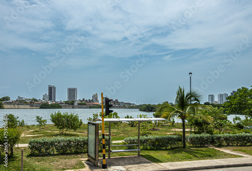 Cartagena, Colombia - July 25, 2023: Public transport stop along Transversal 17 looking over bay water on historic shore walls of old town with few tall buildings under blue cloudscape photo