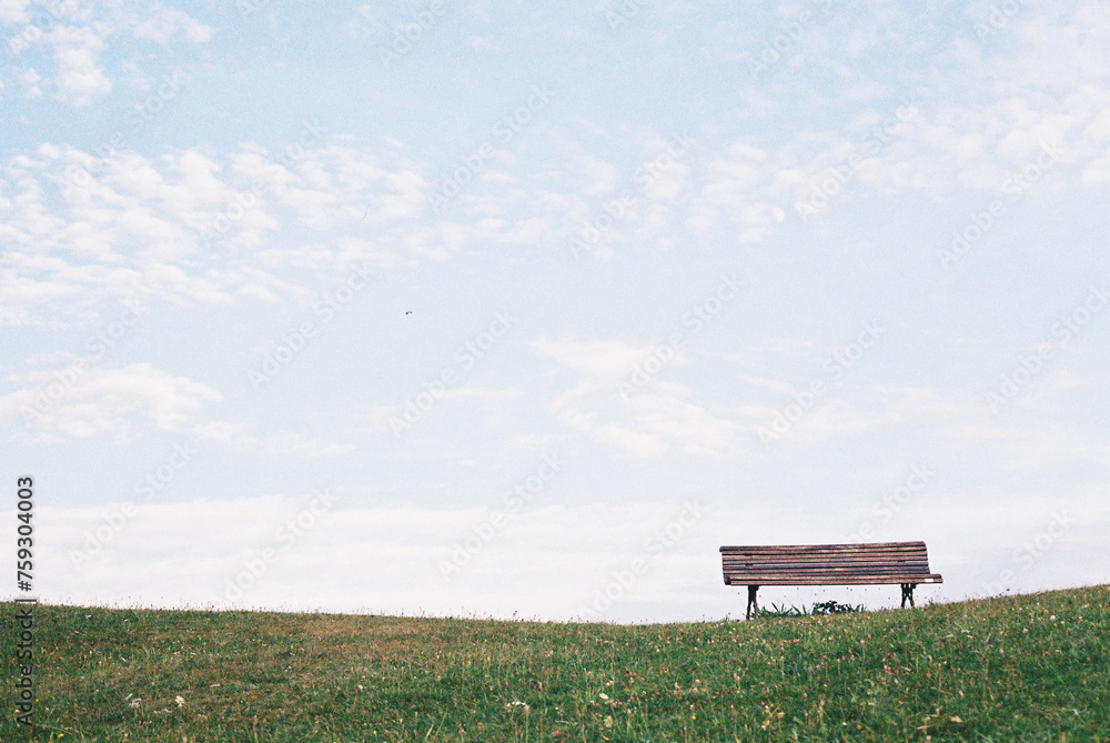 Wooden bench over grass lawn against blue sky in countryside Wooden bench over grass lawn against blue sky in countryside