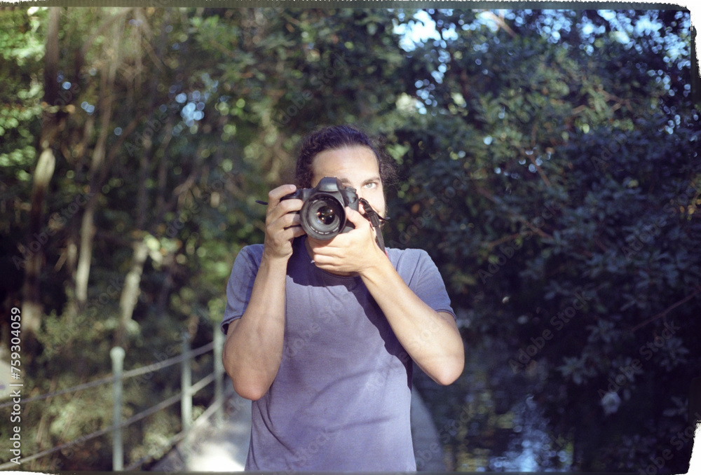 Man taking photo on camera while standing against forest trees Man taking photo on camera while standing against forest trees