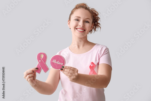 Young woman with ribbon and cookies on light background. Breast cancer awareness concept