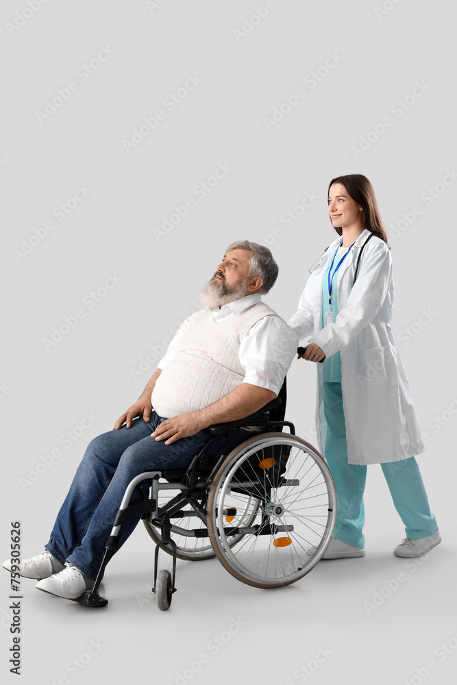 Mature man in wheelchair with nurse on light background Mature man in wheelchair with nurse on light background