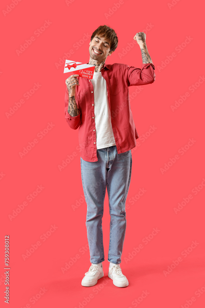 Happy young tattooed man with gift voucher on red background