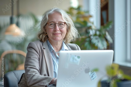 Smiling mid aged business woman in office looking at laptop computer