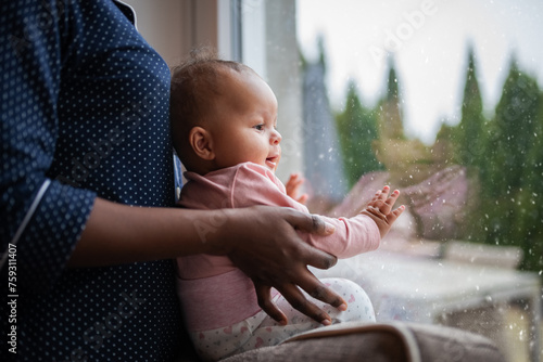 Black woman holds mixed baby near window photo
