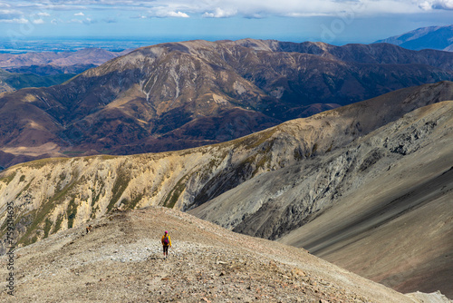 hiker girl enjoys the panorama of southern alps walking alongside a ridge between castle hill peak and foggy peak near porters pass in Korowai / Torlesse Tussocklands Park; climbing in New Zealand photo
