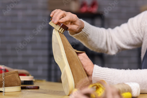 Mature shoemaker brushing shoe at table in workshop, closeup