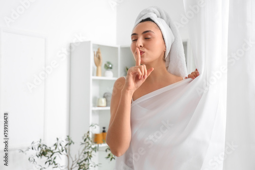 Young woman showing silence gesture behind bathroom curtain at home