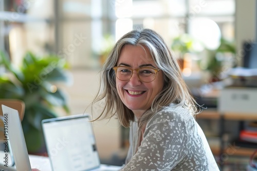 Smiling mid aged business woman in office looking at laptop computer