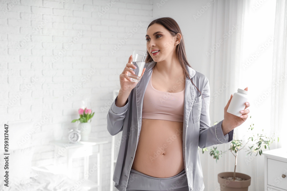 Young pregnant woman with pill bottle and glass of water in bedroom Young pregnant woman with pill bottle and glass of water in bedroom