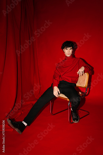 Stylish young male model sitting on chair against red photo