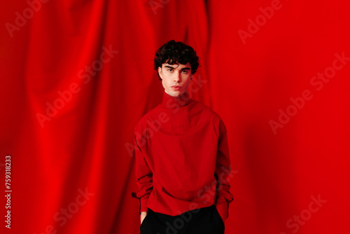 Serious young man standing near red background in studio