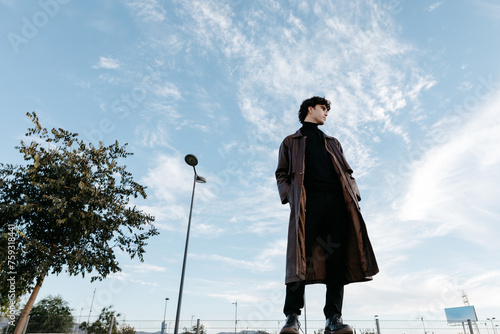 Stylish young man standing against blue sky wearing high neck photo