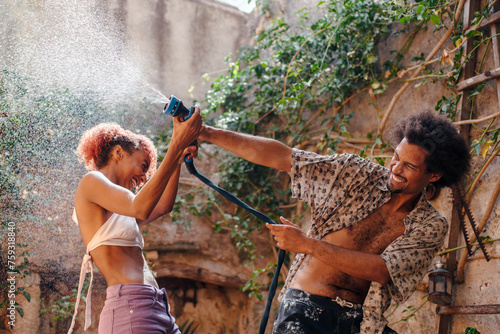 Black couple teasing each other playing with a water hose in summer