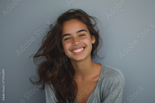 A woman with long hair is smiling and wearing a grey shirt