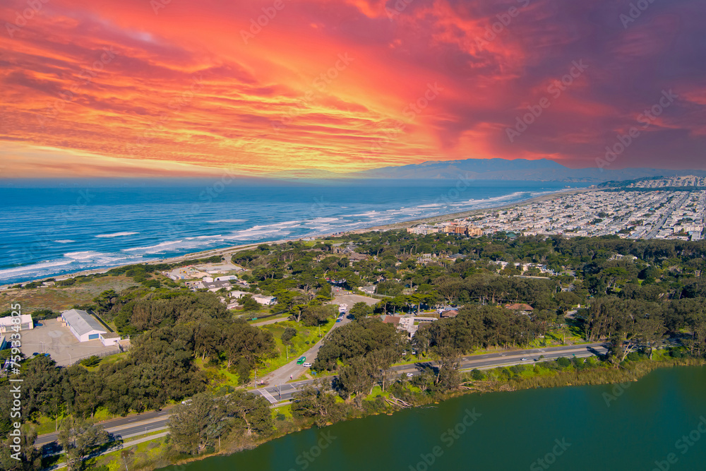 aerial shot of a beautiful spring landscape at Lake Merced with vast blue ocean water a sandy beach, green trees and grass and cars on the street in San Francisco California USA