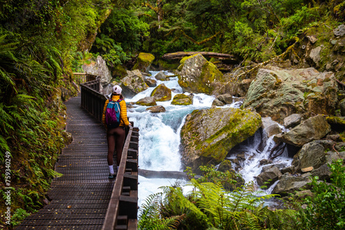 hiker girl admiring a rushing river with waterfalls in fiordland national park, new zealand south island, hiking trail to lake marian