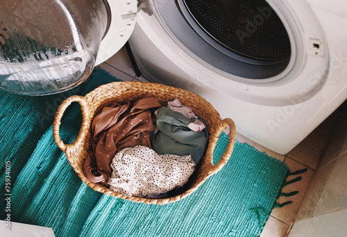  A basket with laundry by a washing machine.
