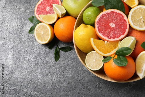 Different fresh citrus fruits and leaves in bowl on grey textured table  flat lay. Space for text