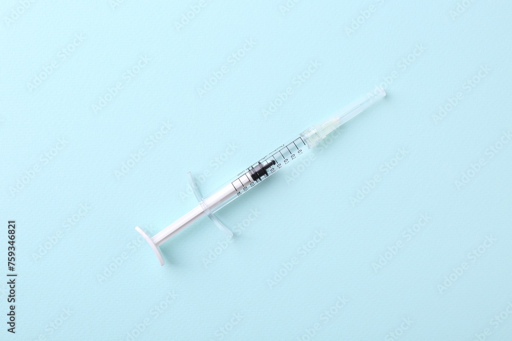 Injection cosmetology. One medical syringe on light blue background, top view Injection cosmetology. One medical syringe on light blue background, top view