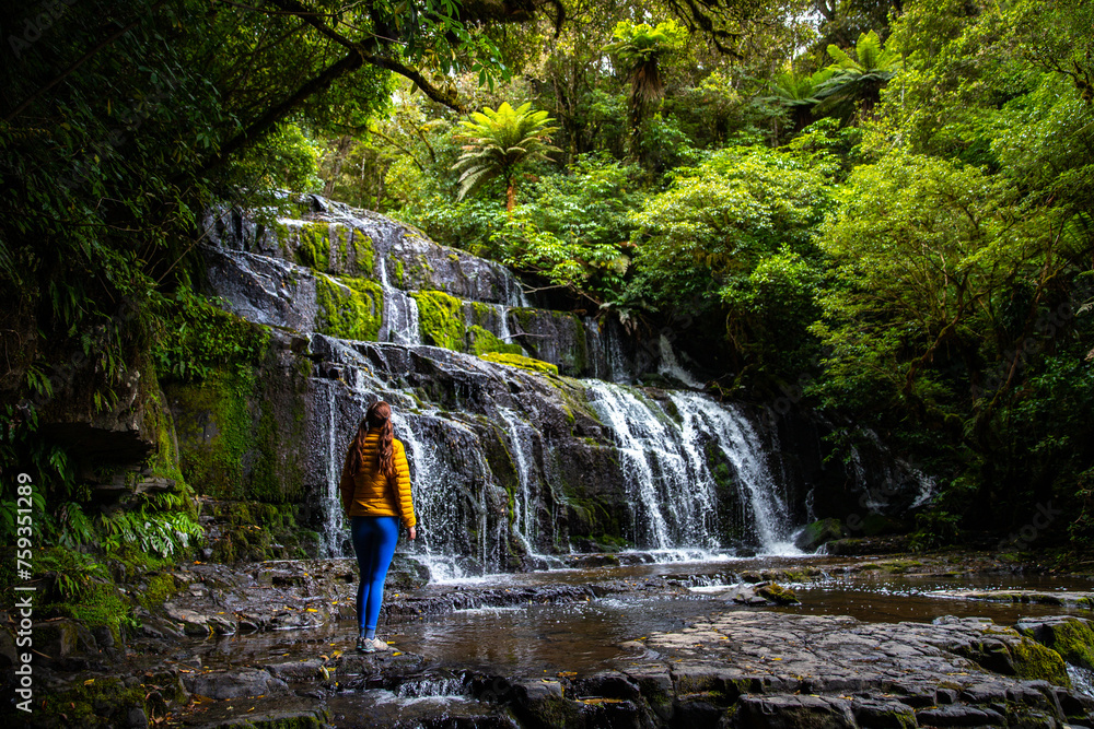 lovely hiker girl stands and admires mighty Purakaunui Falls surrounded by stunning native rainforest in Catlins Forest Park, Otago, New Zealand, hidden gems of NZ south island lovely hiker girl stands and admires mighty Purakaunui Falls surrounded by stunning native rainforest in Catlins Forest Park, Otago, New Zealand, hidden gems of NZ south island