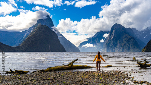 Happy girl in yellow jacket admires famous Milford Sound fiord and mighty mountains densely covered with vegetation in Fiordland National Park, Southland, New Zealand