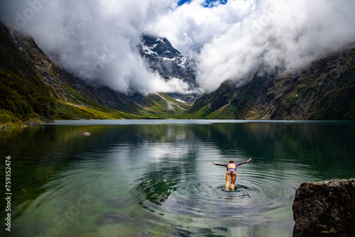 pretty girl in a swimsuit diving into famous alpine lake marian surrounded with mountains lake in fiordland national park near milford sound, new zealand, southland, south island