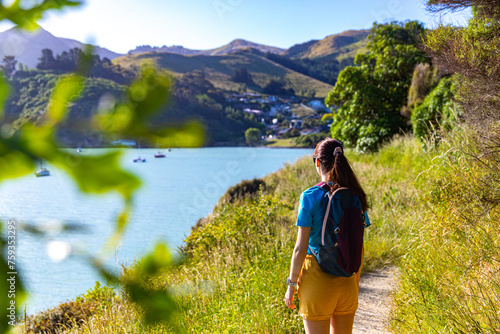 pretty backpacker girl enjoys the coastal walk between pony point and lyttelton near christchurch, canterbury, new zealand south island; hiking on the coast with the view of banks peninsula