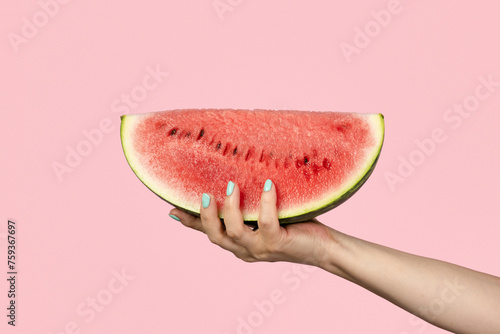 Female hand holding slice of watermelon on pink background photo