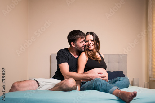 Affectionate pregnant couple sitting on bed photo