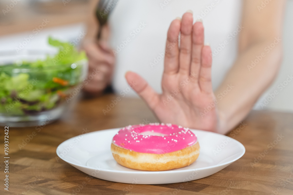 Woman on dieting for good health concept. Close up female using hand push out her favourite donut and choose salad vegetables for good health.