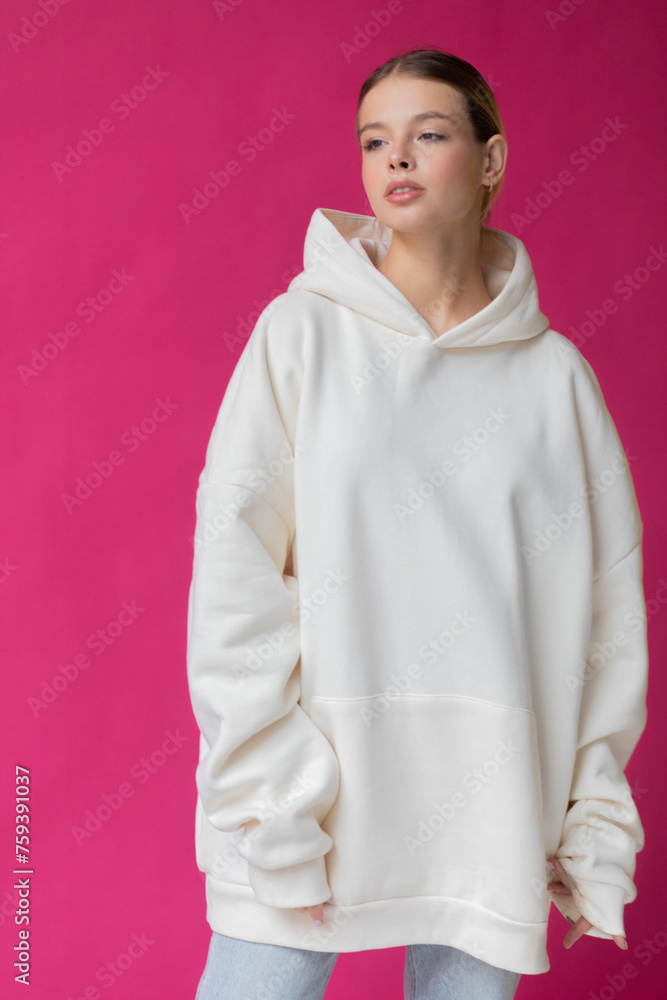 Beautiful blonde woman in a white hoodie and blue jeans posing on a pink background Beautiful blonde woman in a white hoodie and blue jeans posing on a pink background