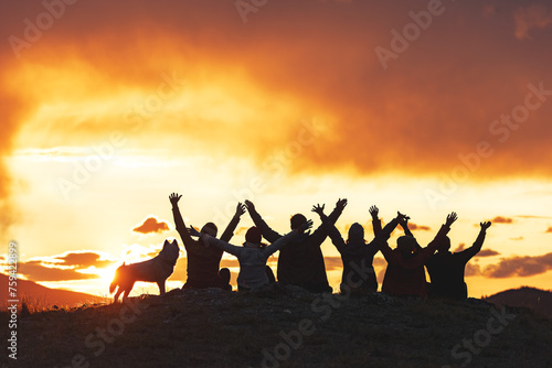 Big group of happy friends are sitting with open arms against sunset sky © cppzone