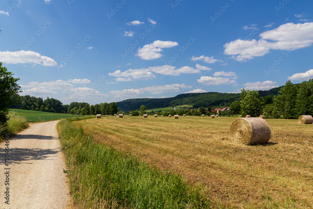 Rural scene with round hay bales, hill panorama and hiking path near village Wannbach in Franconian Switzerland, Germany