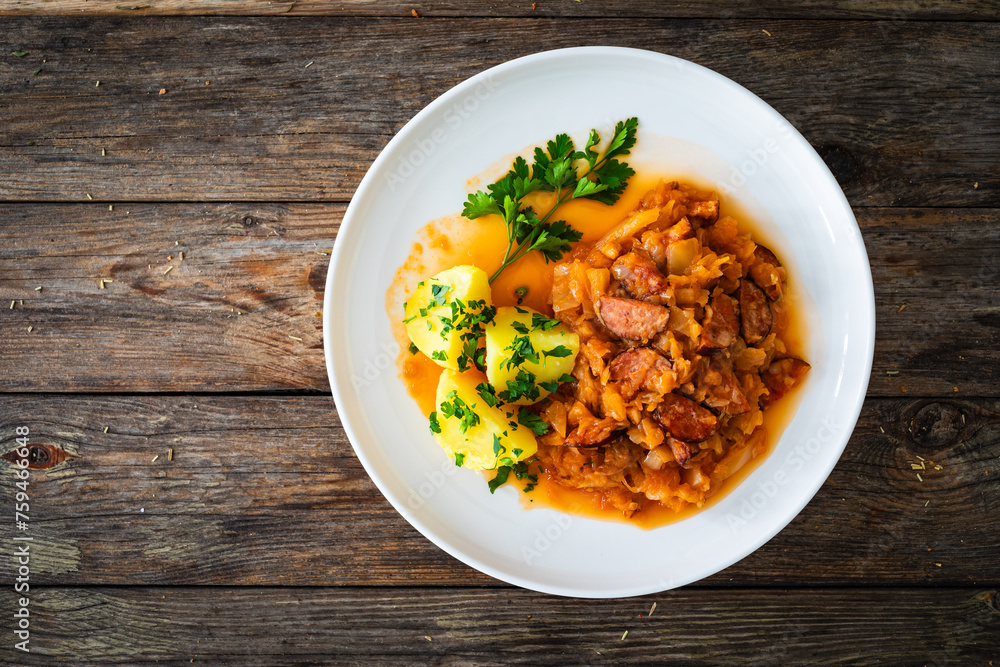 Bigos - cooked cabbage with sliced sausage and boiled potatoes on wooden table Bigos - cooked cabbage with sliced sausage and boiled potatoes on wooden table