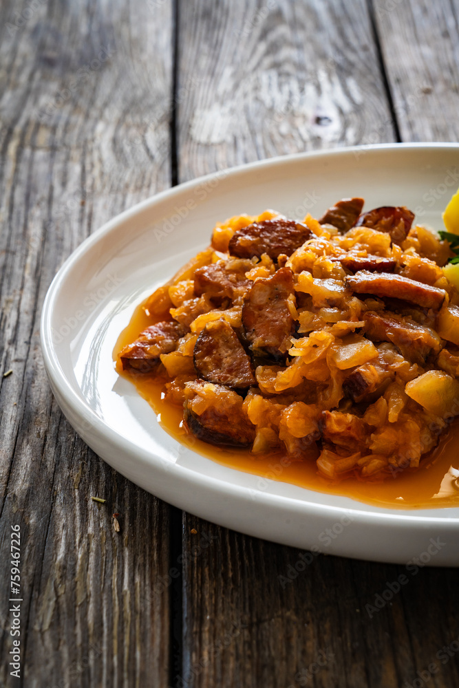 Bigos - cooked cabbage with sliced sausage and boiled potatoes on wooden table Bigos - cooked cabbage with sliced sausage and boiled potatoes on wooden table