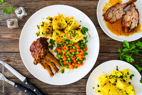 Veal ribs, boiled potatoes, peas and carrots on wooden table
