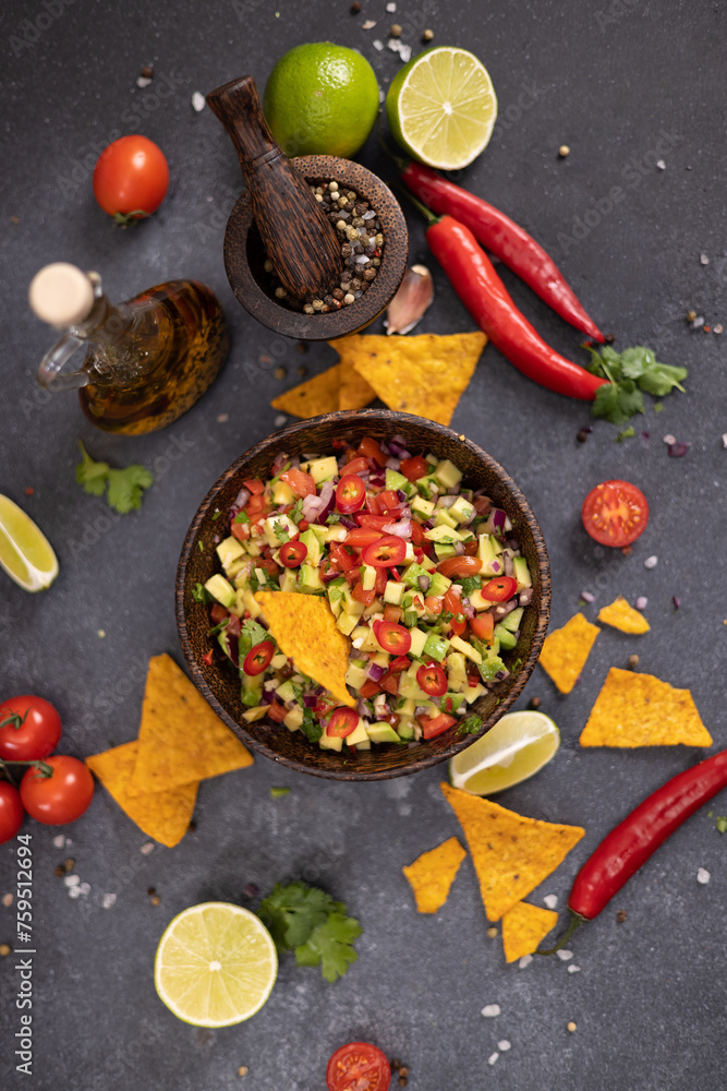 traditional salsa dip snack in wooden bowl and corn nacho chips on a table with ingredients