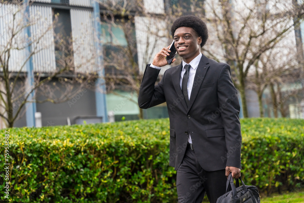 African businessman walking along the street using phone African businessman walking along the street using phone