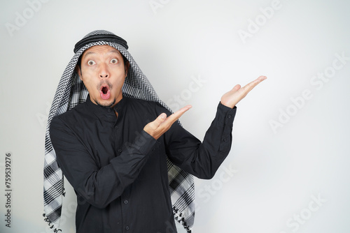 Wow face shocked expression Asian Muslim man wearing Arab turban sorban pointing hand finger at empty space photo