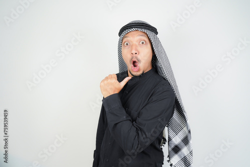 Wow face shocked expression Asian Muslim man wearing Arab turban sorban pointing hand finger at empty space photo