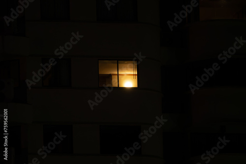 A window in a building is lit up by a light. The room is dark and the window is the only source of light